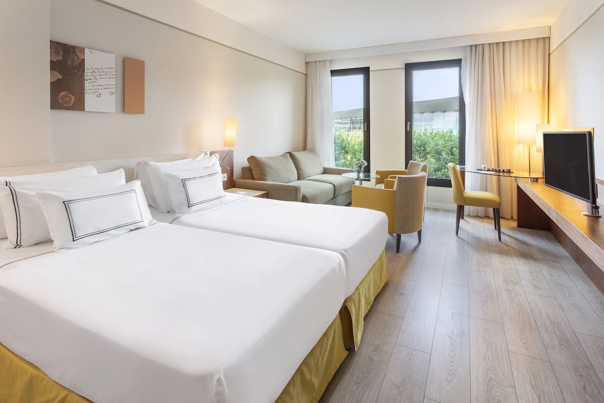 Habitación de hotel con dos camas, un sofá, un televisor y una ventana con vistas a zonas verdes.