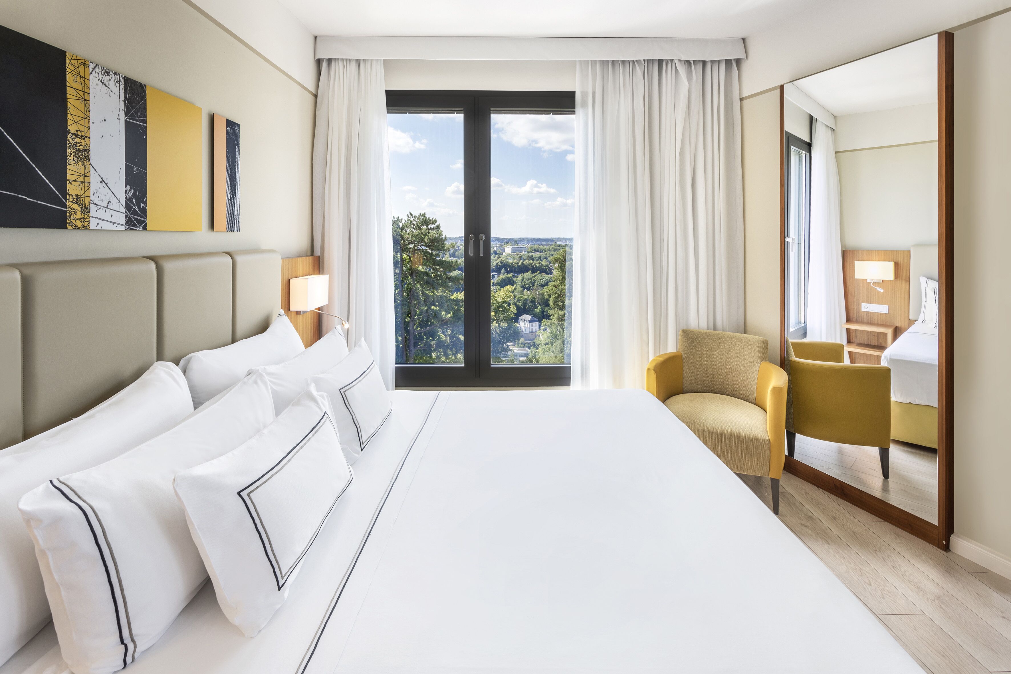 Une chambre d’hôtel avec un grand lit, une chaise, un bureau et une vue sur l’extérieur.