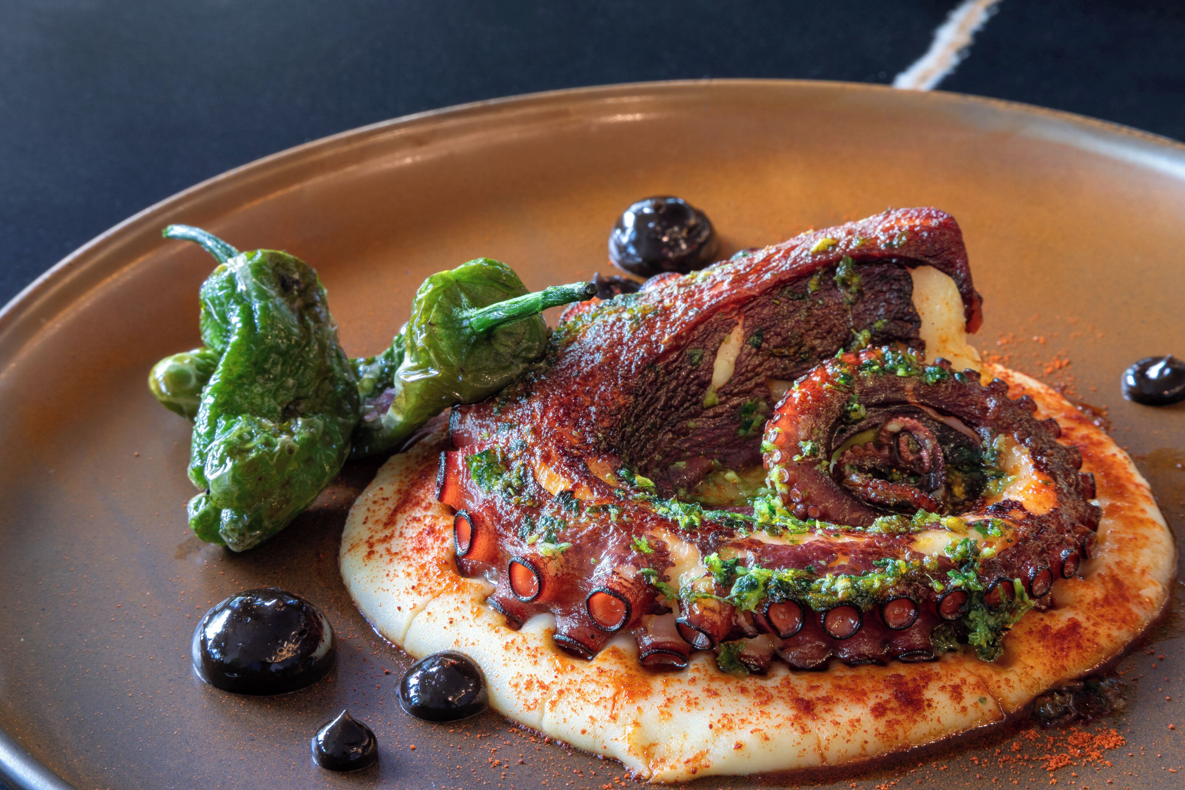 A plate with octopus, olives, and a green vegetable.