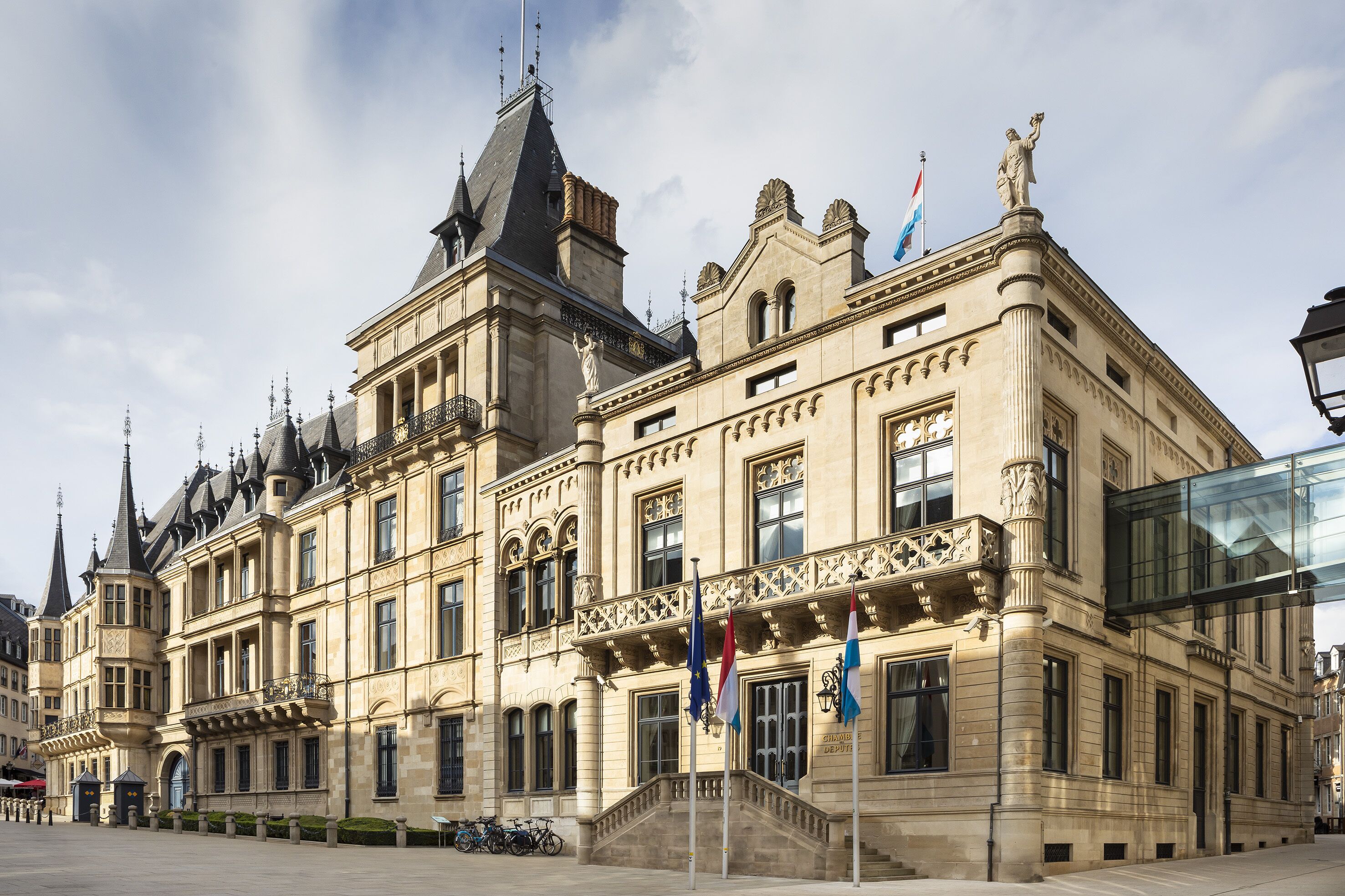 A historic building with ornate architecture, multiple flags, and a prominent statue on the roof.