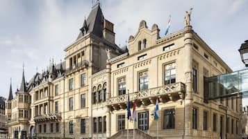 Un bâtiment historique à l’architecture riche et ornée, orné de nombreux drapeaux et surmonté d’une statue imposante.