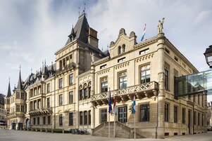 Un edificio histórico con arquitectura ornamentada, varias banderas y una estatua destacada en el tejado.