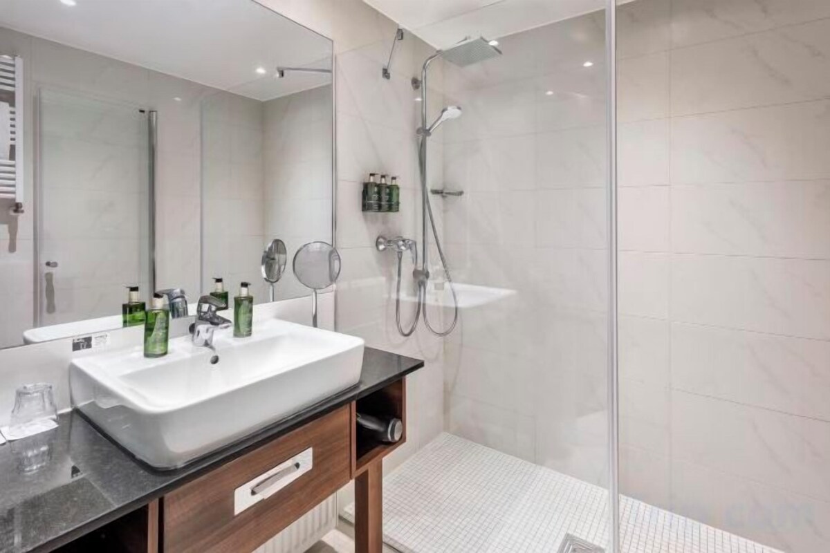 Een moderne badkamer met een groot wit wastafelmeubel, een spiegel en een douchecabine met glazen wanden.