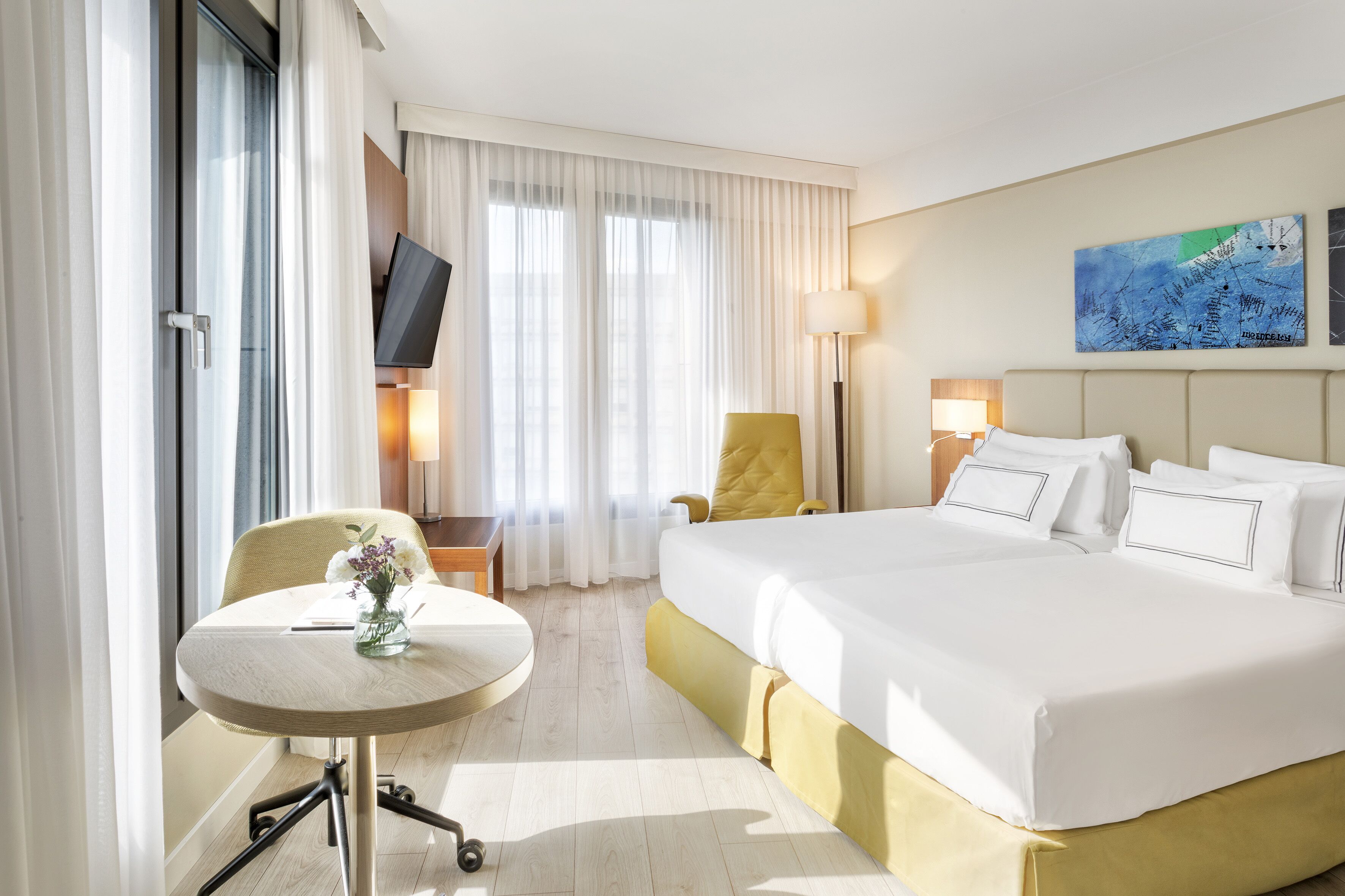 Habitación de hotel con cama, escritorio, silla, televisor y un cuadro en la pared.