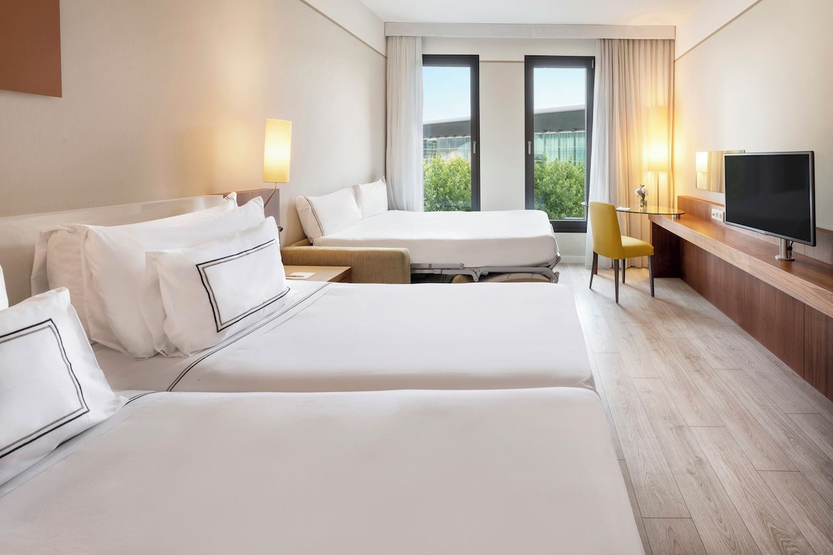 Une chambre d’hôtel avec deux lits, un bureau, une télévision et une vue sur la verdure par les fenêtres.