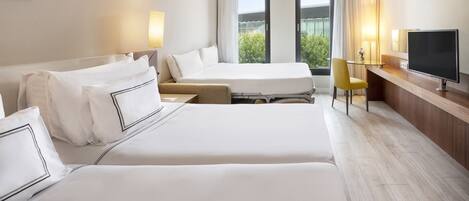 A hotel room with two beds, a desk with a TV, and a view of greenery outside.