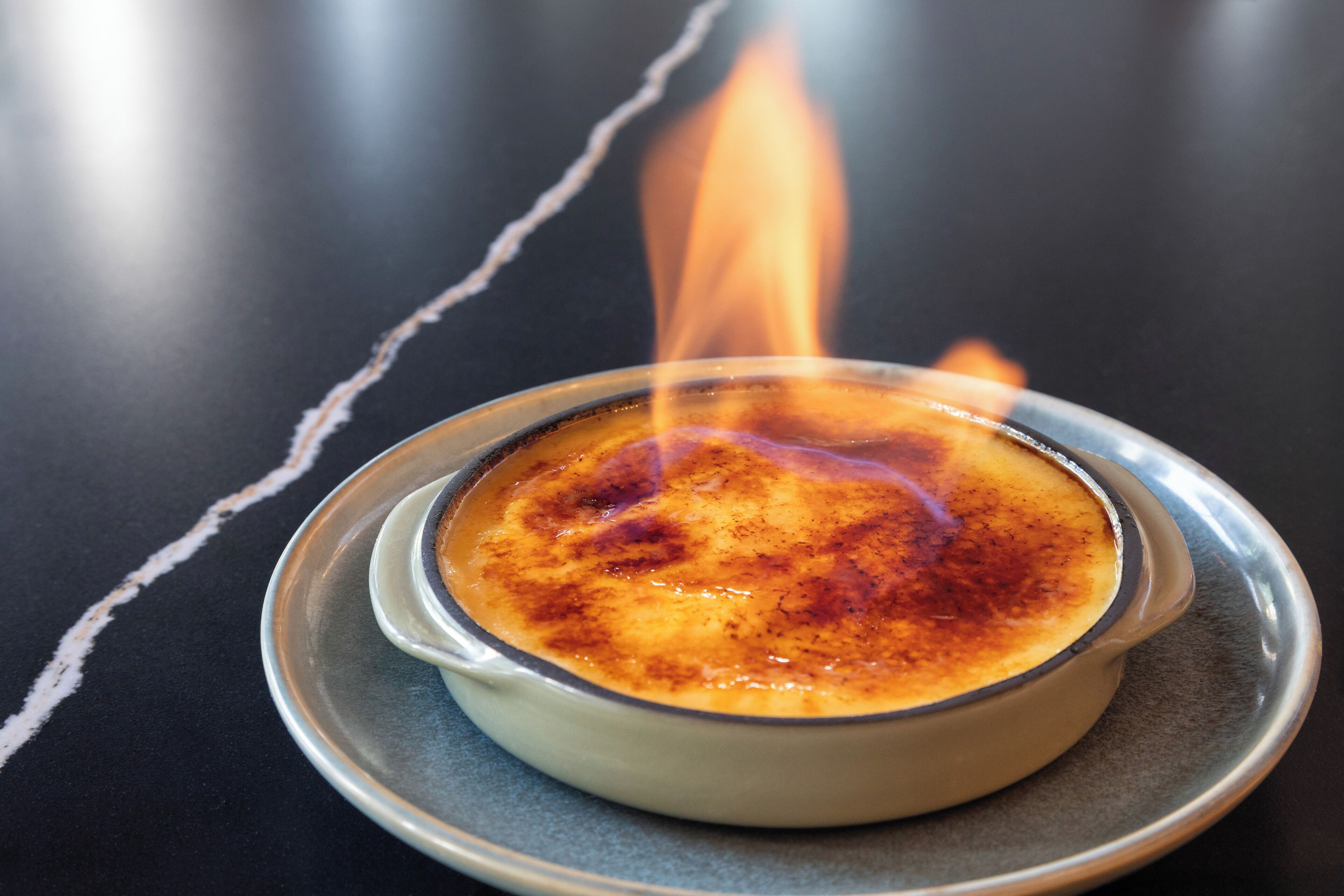 A crème brûlée on a plate with a flame above it.