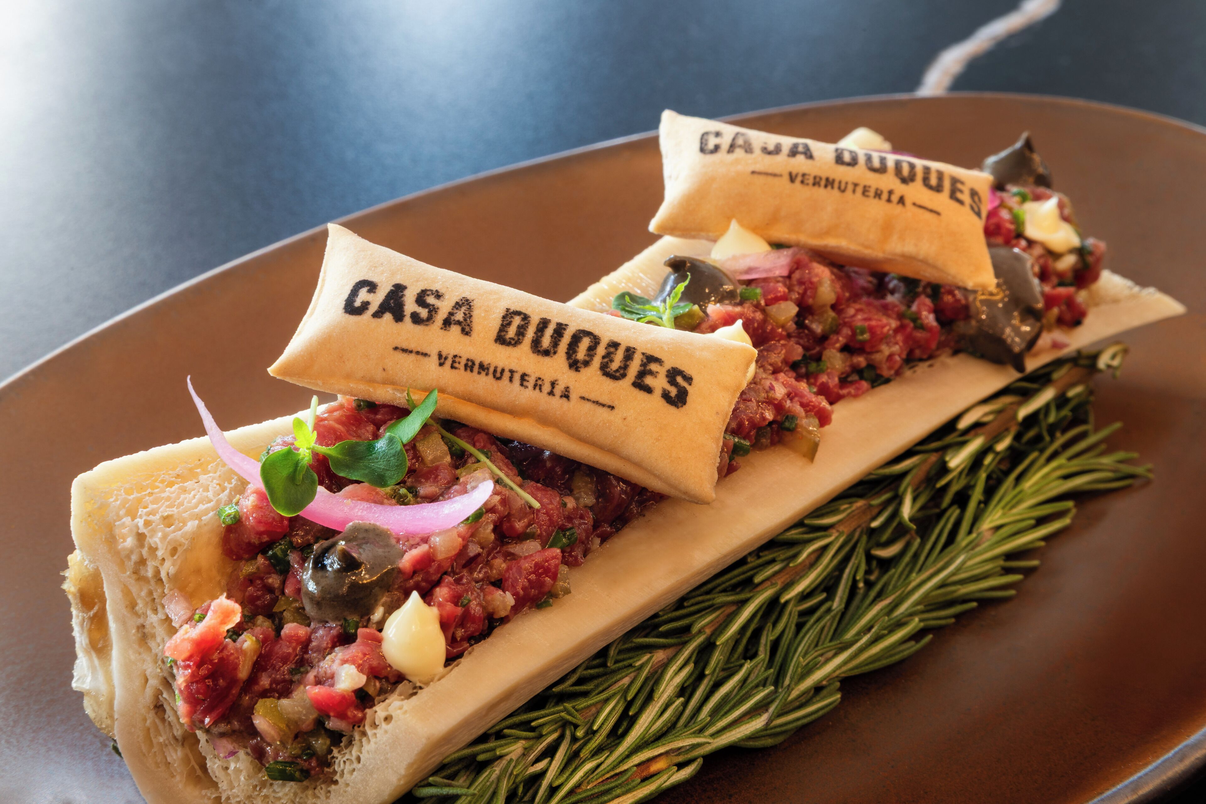 Two sandwiches on a plate with a rosemary garnish.