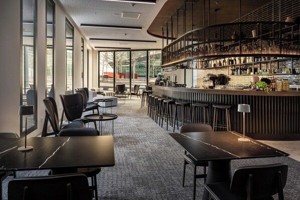 Zona de bar moderna con mostrador curvo, asientos y vistas al exterior.
