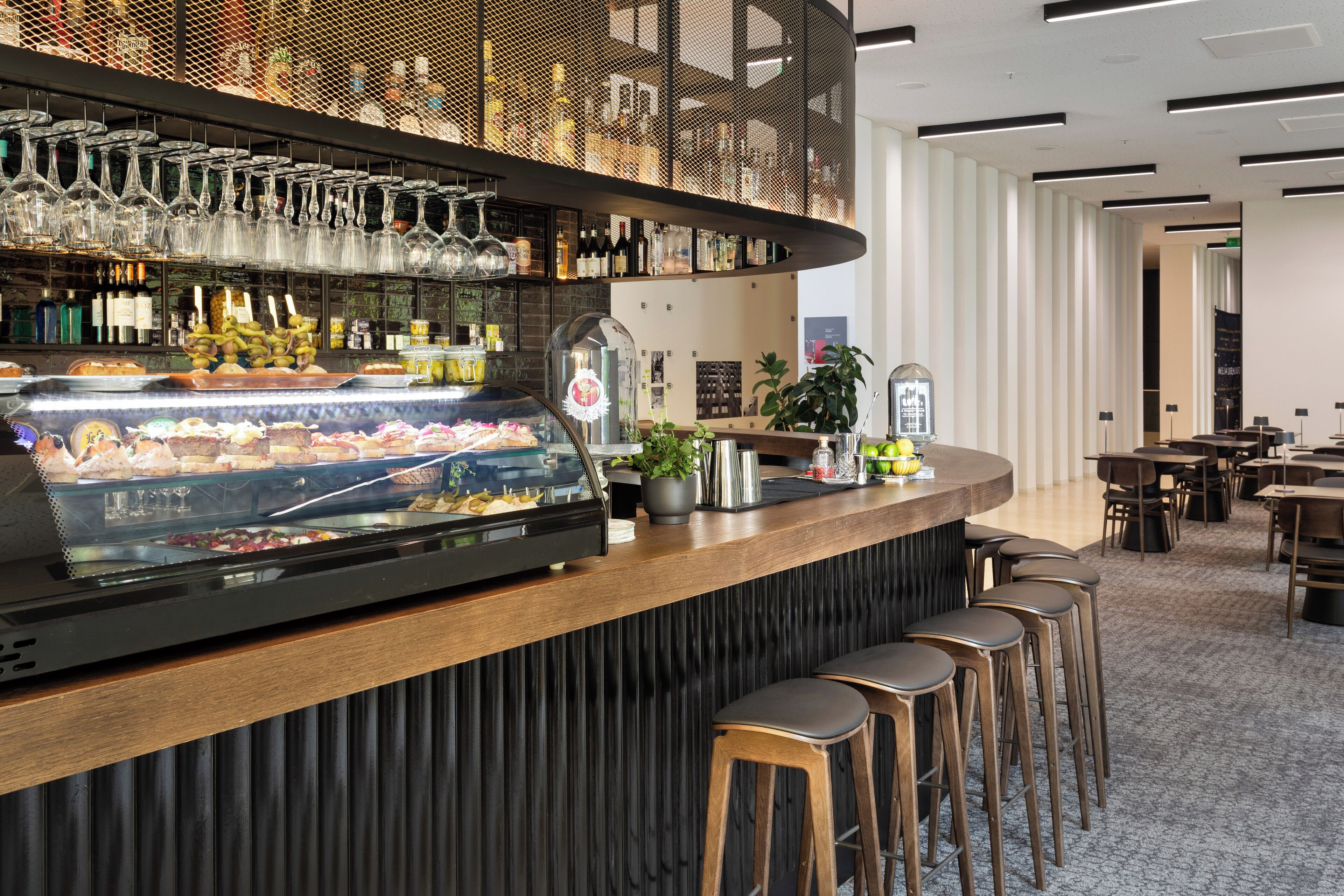 Zona de bar con vitrina de comida, selección de botellas y copas colgantes.