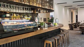Zona de bar con vitrina de comida, selección de botellas y copas colgantes.