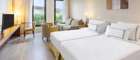 Ein Hotelzimmer mit zwei Betten, einem Schreibtisch mit Fernseher, einem Sessel und einer Couch.