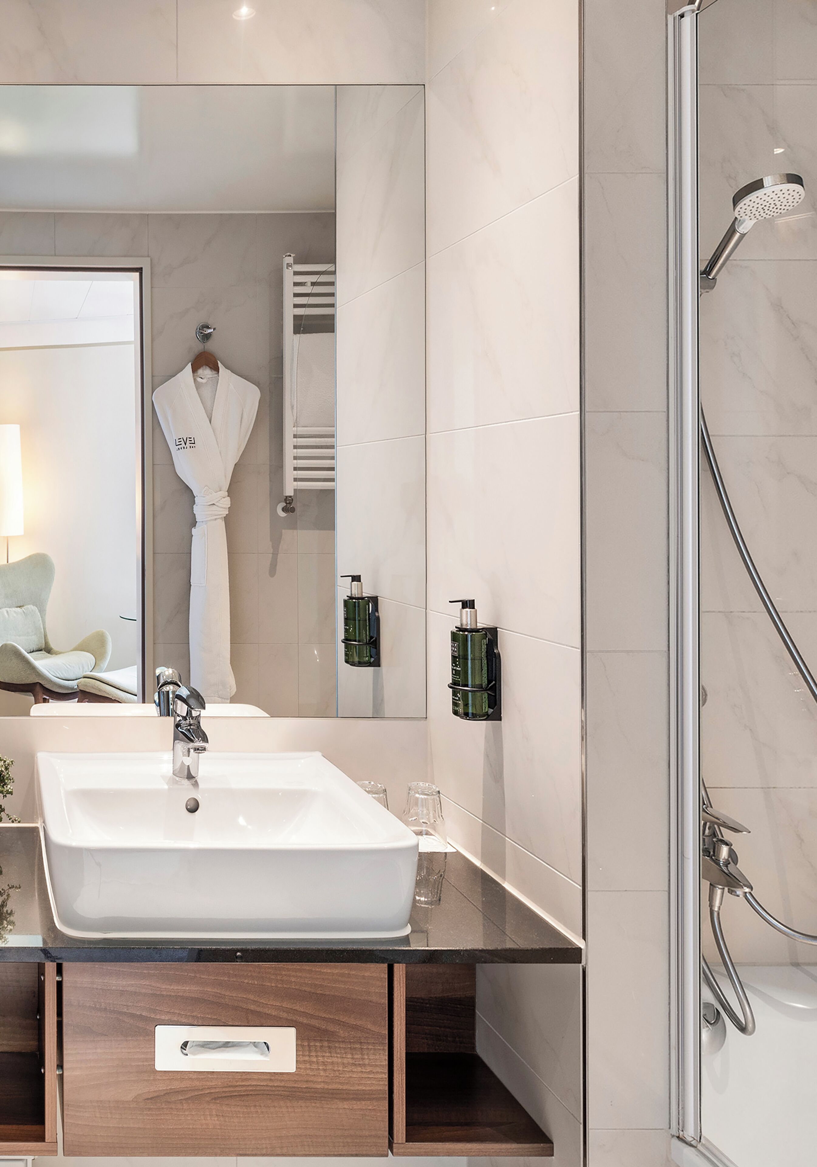 Une salle de bain moderne avec un grand miroir, un lavabo blanc, une cabine de douche en verre et un porte-serviettes.