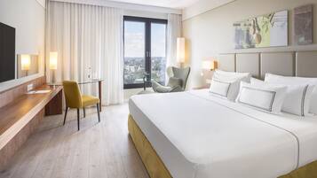 A hotel room with a large bed, a desk, a chair, and a view of the city through a large window.