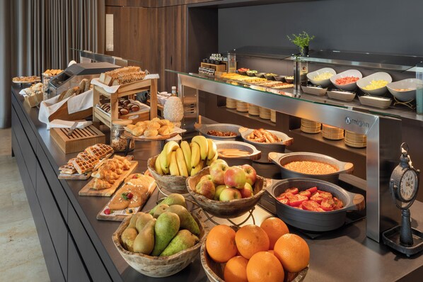 Un bufé con diversas frutas, pasteles y pan.