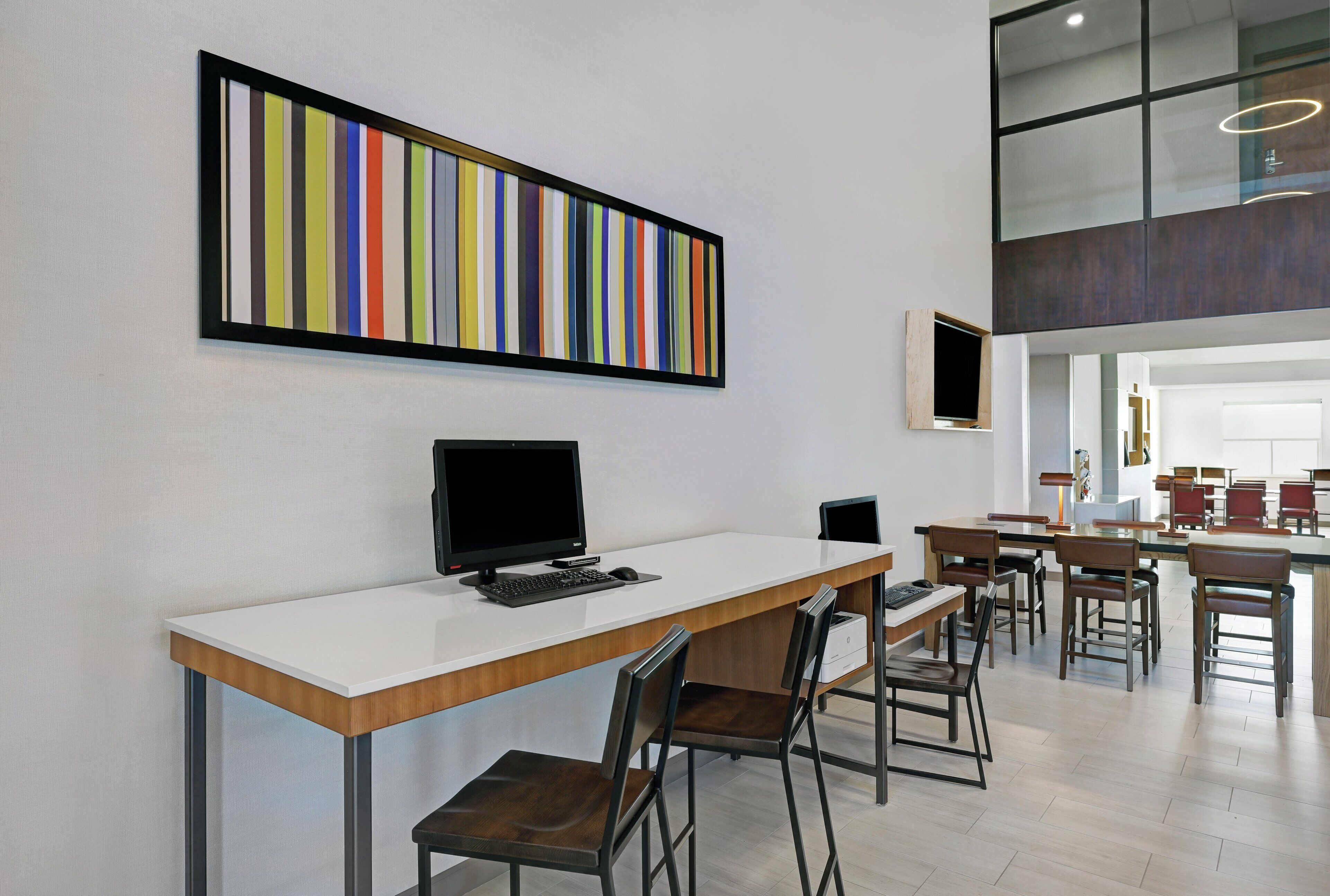 A modern office space with a long desk, chairs, a computer, and a colorful abstract painting on the wall.