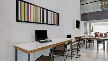 A modern office space with a long desk, chairs, a computer, and a colorful abstract painting on the wall.