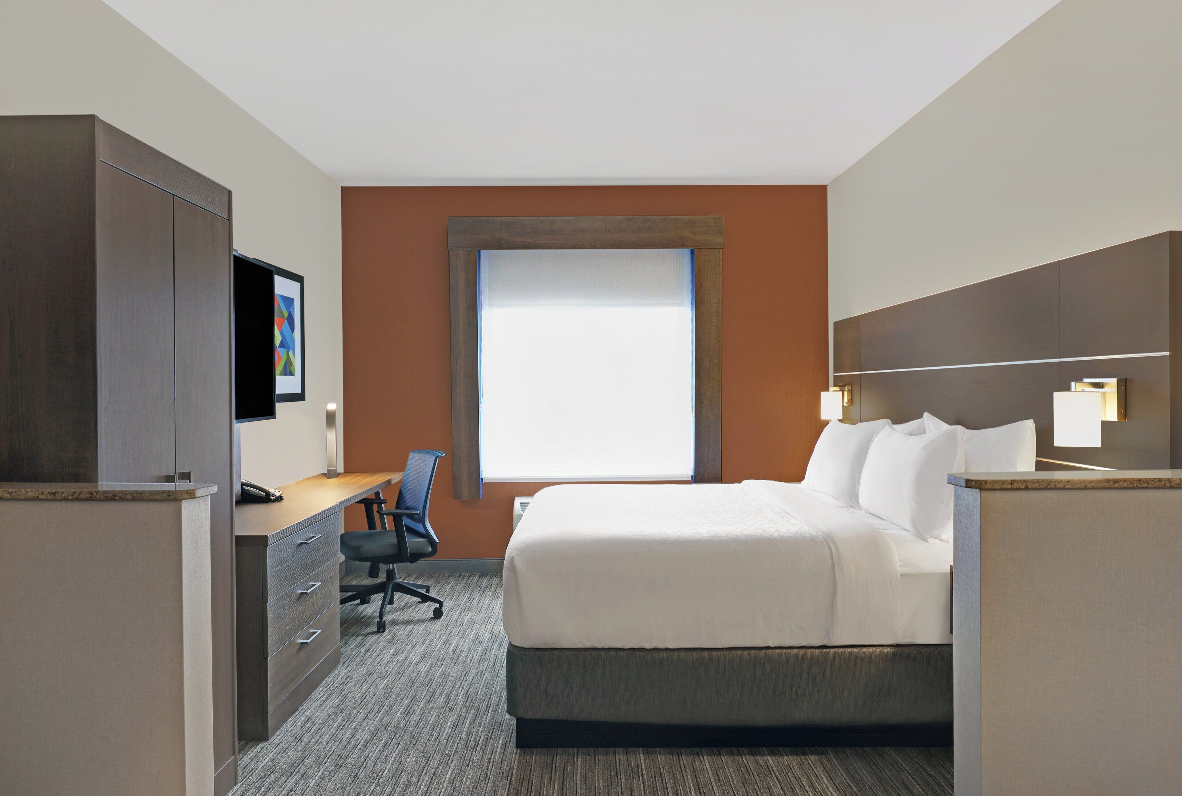 A hotel room with a bed, desk, chair, and a TV.