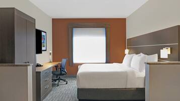 A hotel room with a bed, desk, chair, and a TV.