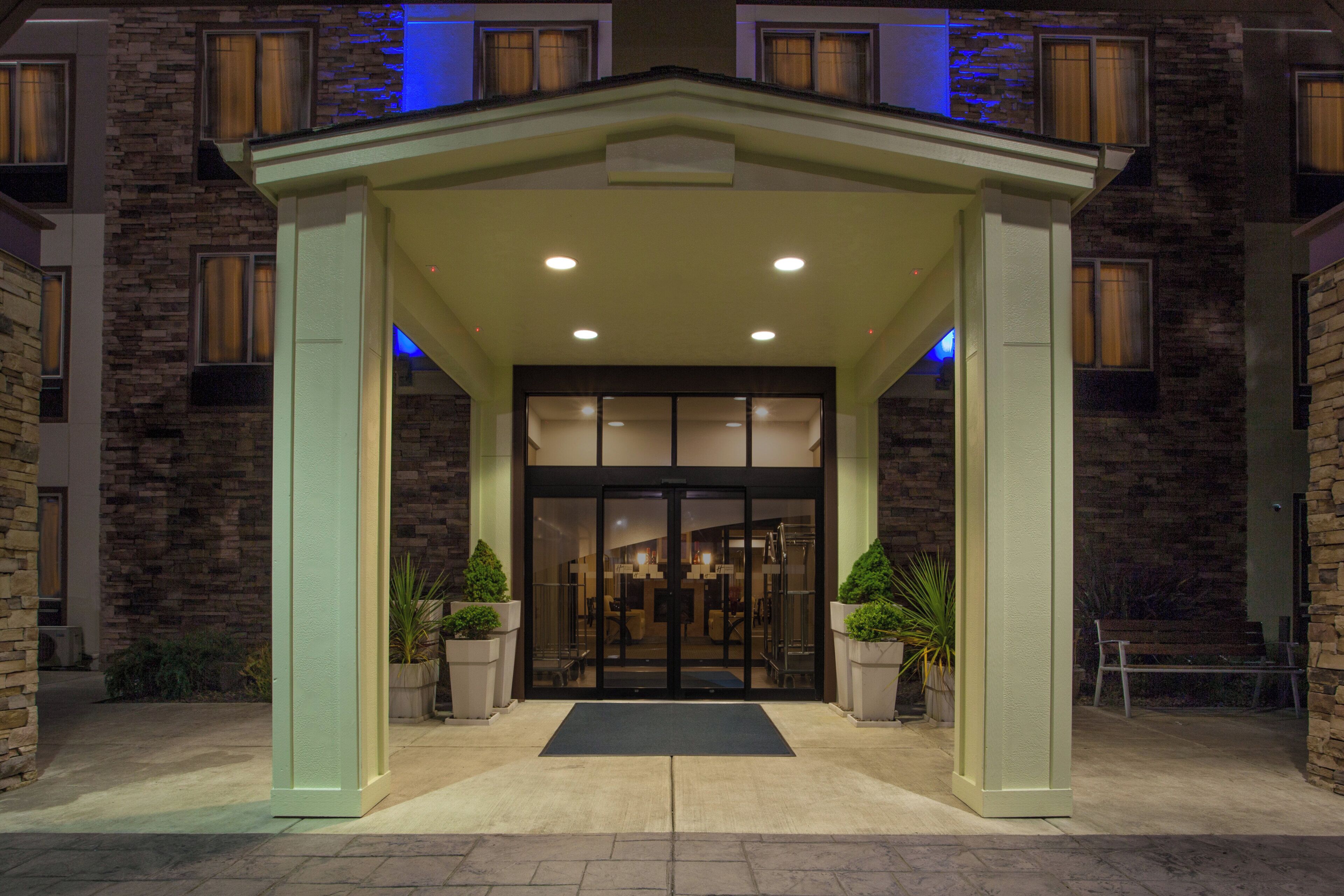 A building entrance with a stone facade, a covered entrance area, and potted plants.