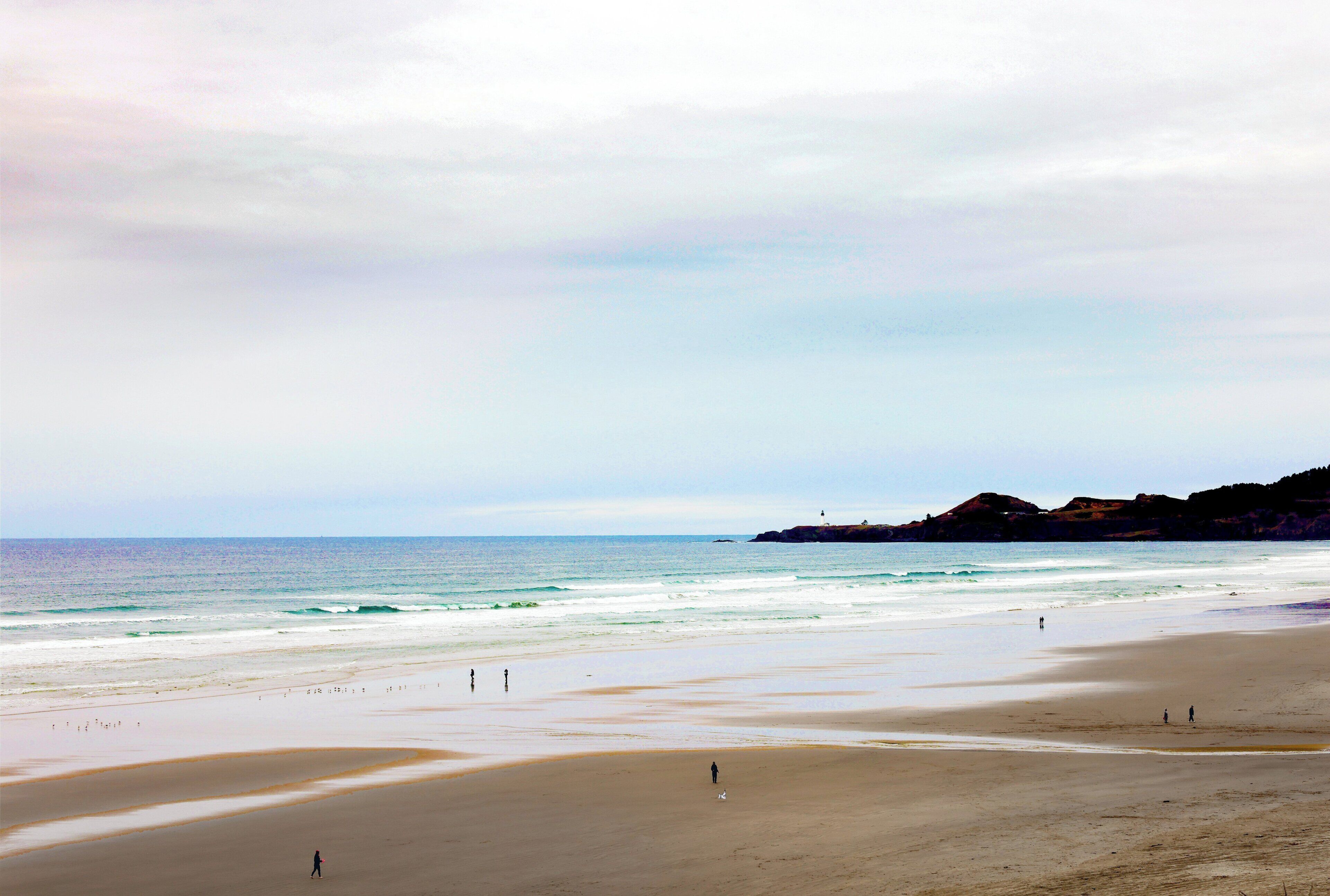 Una platja amb un far, mar tranquil·la i turons a la distància.