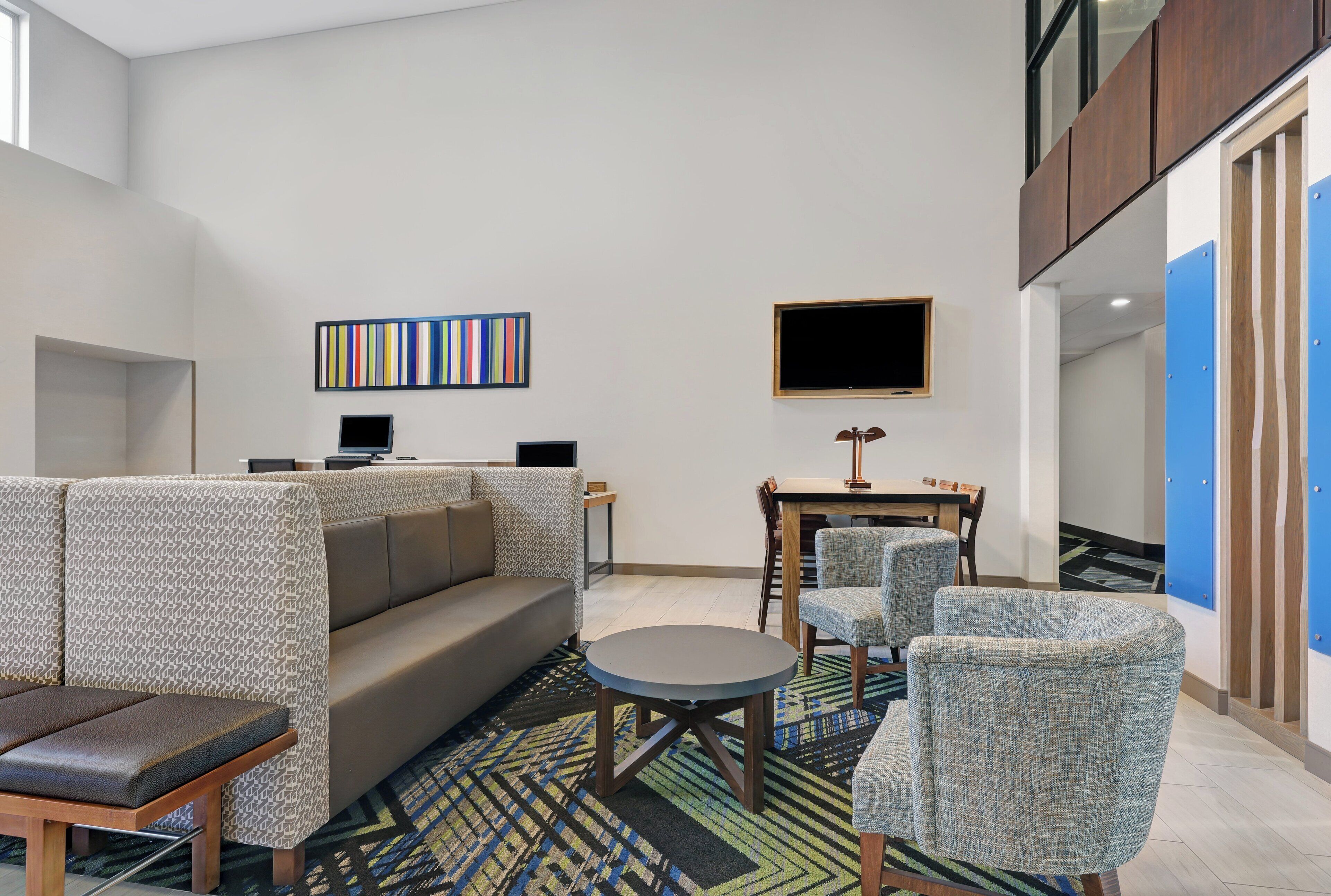 A modern lounge area with a sofa, chairs, a small table, and a flat-screen TV mounted on the wall.