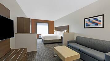 Habitación de hotel con cama, sofá, televisión, escritorio y un cuadro en la pared.