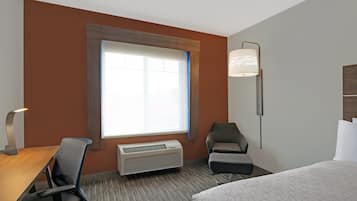 Una habitación de hotel con un ventanal grande, un escritorio con silla, una cama y una lámpara de pie.