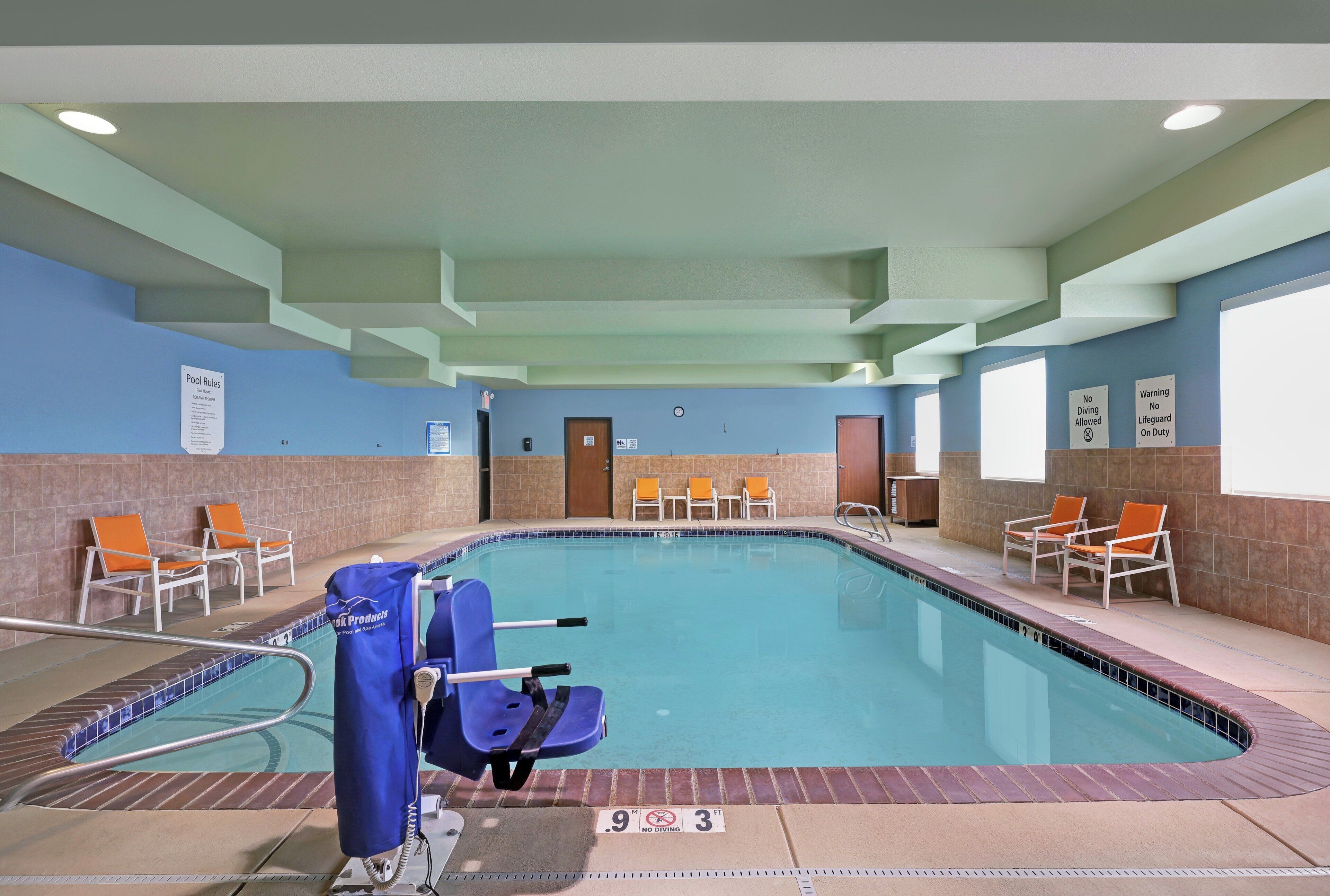 An indoor swimming pool with lounge chairs, a lifeguard sign, and pool rules posted on the wall.