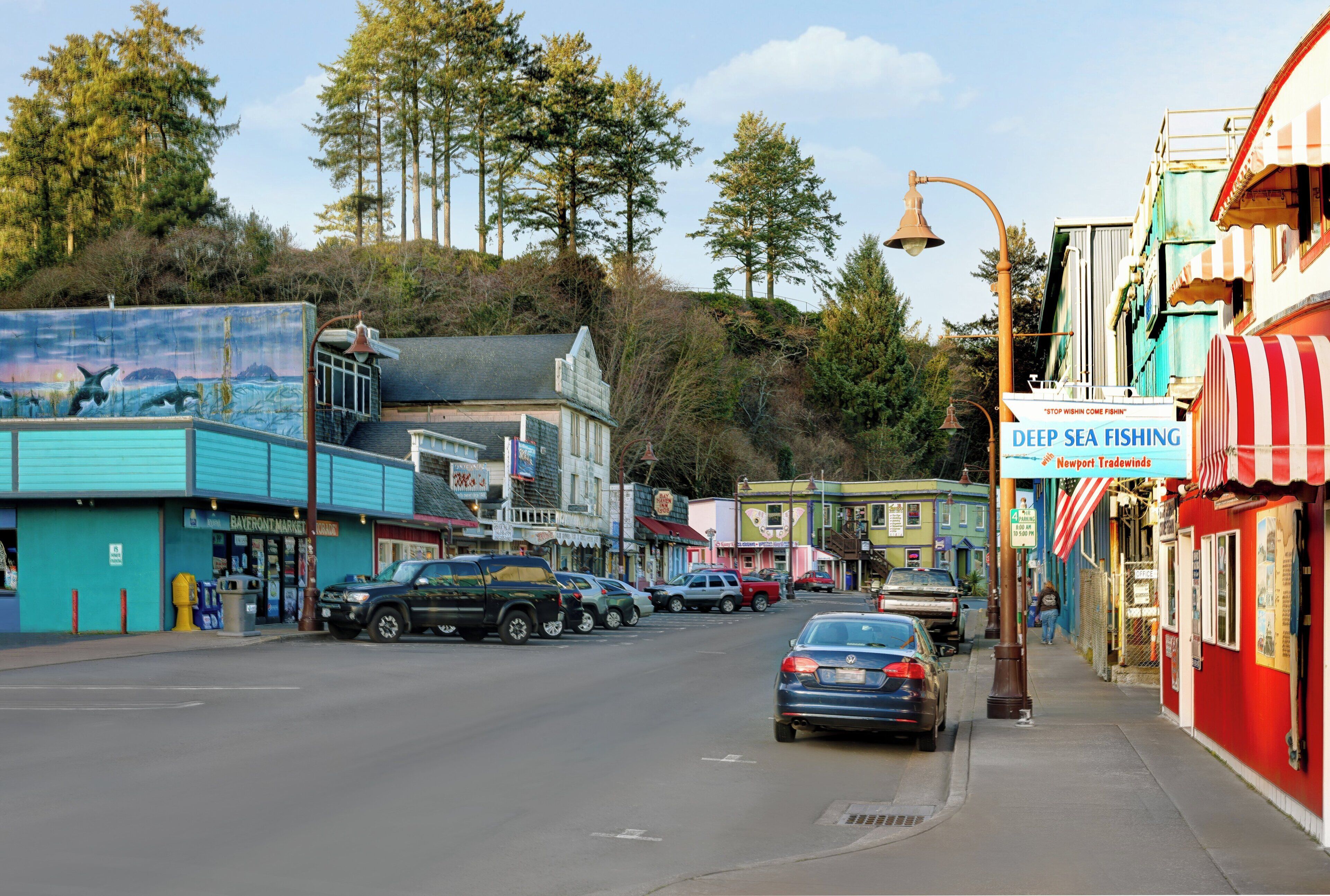 A coastal town street with buildings, parked cars, and a sign for 'Deep Sea Fishing'.