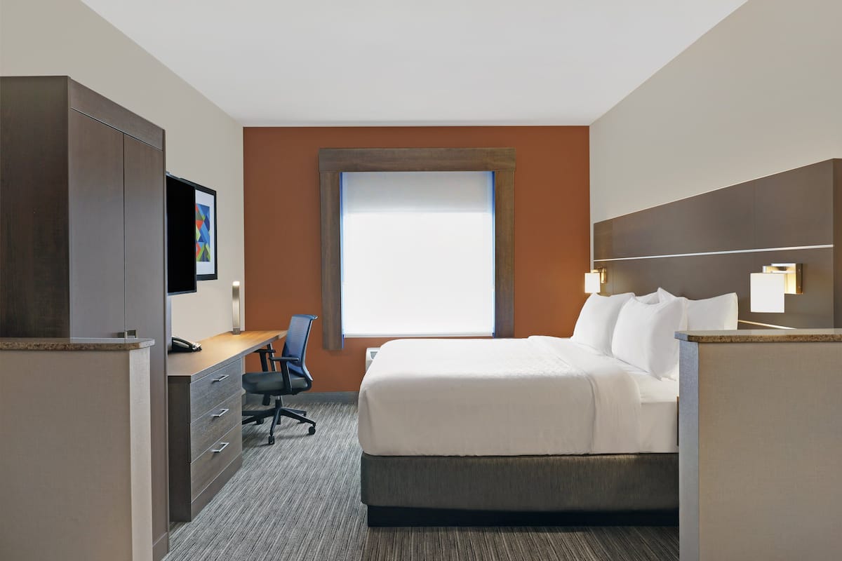 A hotel room with a bed, desk, chair, and a large window.