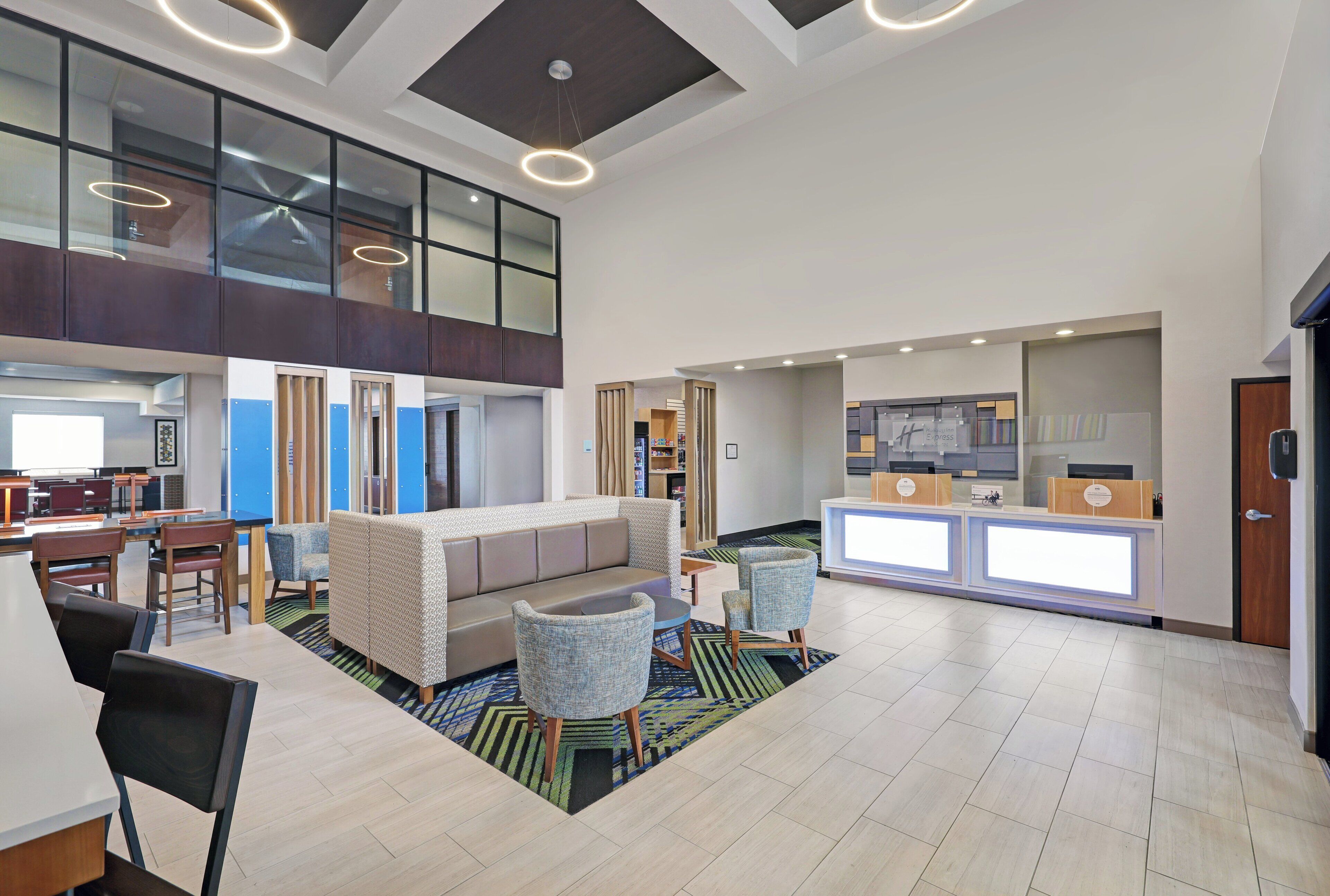 Un hall d’entrée spacieux avec un plafond haut, un coin salon avec un canapé et des fauteuils, un comptoir d’accueil et une vue sur l’étage supérieur grâce à de grandes fenêtres.