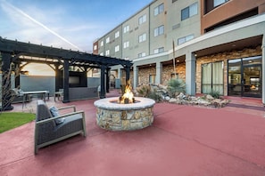Un patio con una fogata de piedra, mobiliario exterior y un área de terraza cubierta.