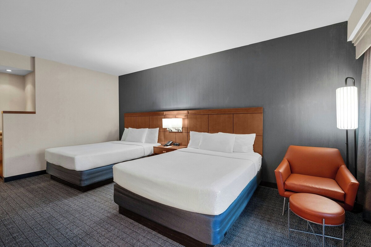 Ein Hotelzimmer mit zwei Betten, einem Sessel, einem Nachttisch und einer Lampe.