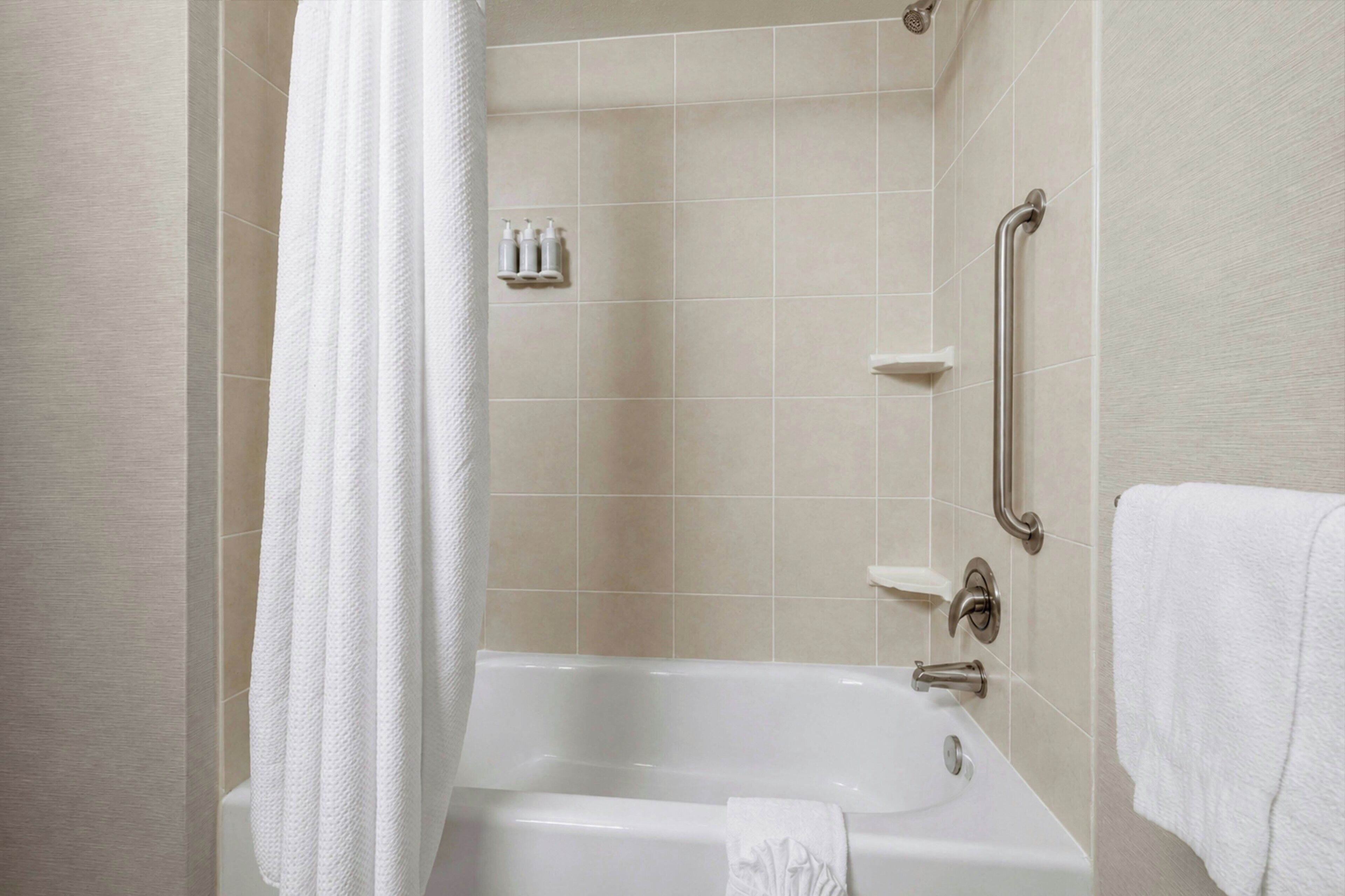 Une salle de bain équipée d’une baignoire, d’un rideau de douche, d’une barre d’appui et d’un porte-serviettes.