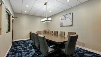 A conference room with a large table, chairs, a ceiling light, and a framed artwork on the wall.