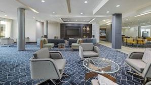 Un hall d’entrée spacieux, doté d’un tapis à motifs, de coins salon, d’un téléviseur à écran plat et d’un espace repas.