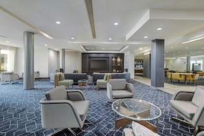 Un lobby espacioso con alfombra estampada, zonas de estar, un televisor de pantalla plana y un comedor.
