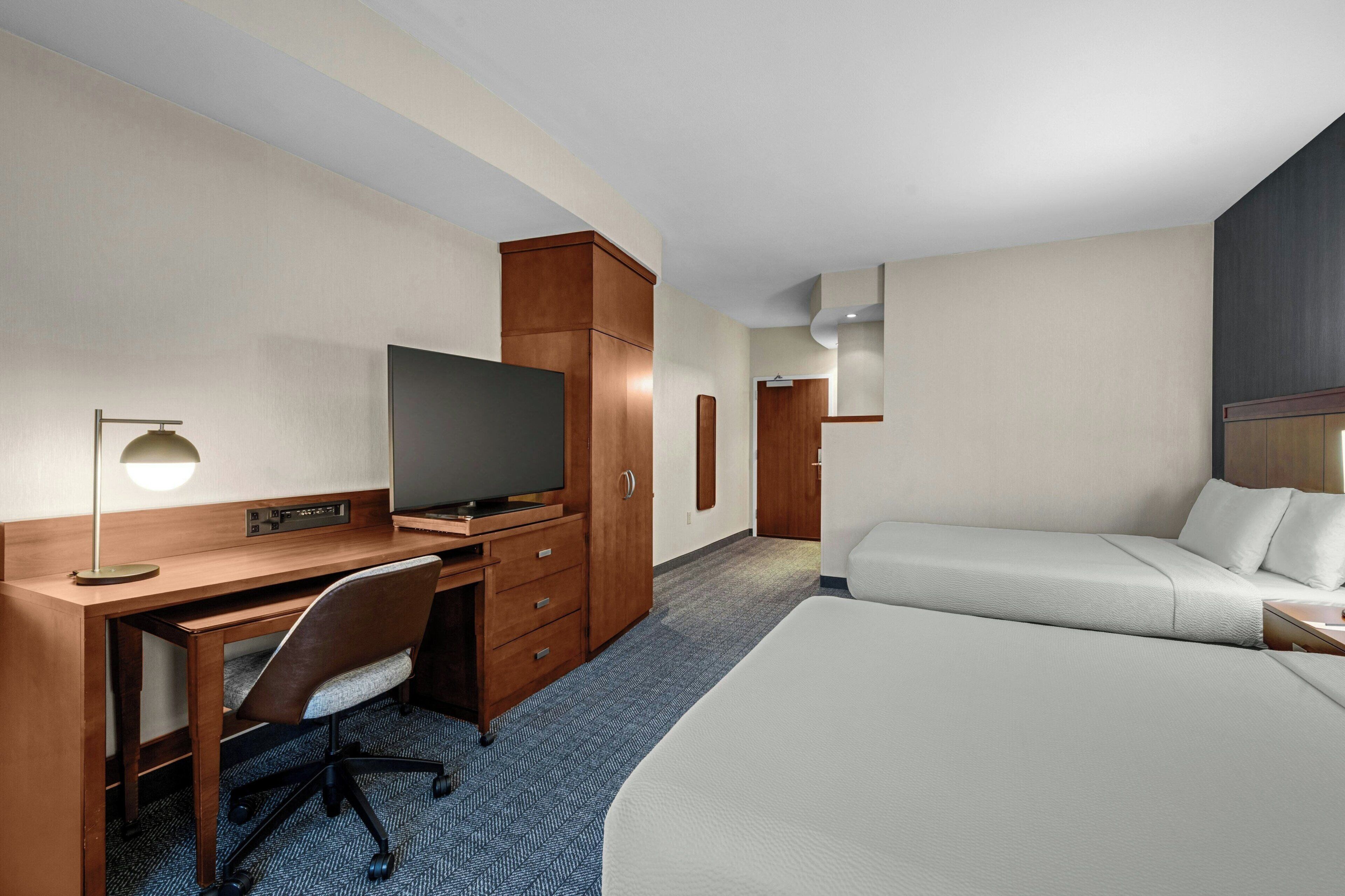 A hotel room with a bed, a desk with a television, a chair, a wardrobe, and a door leading to another room.