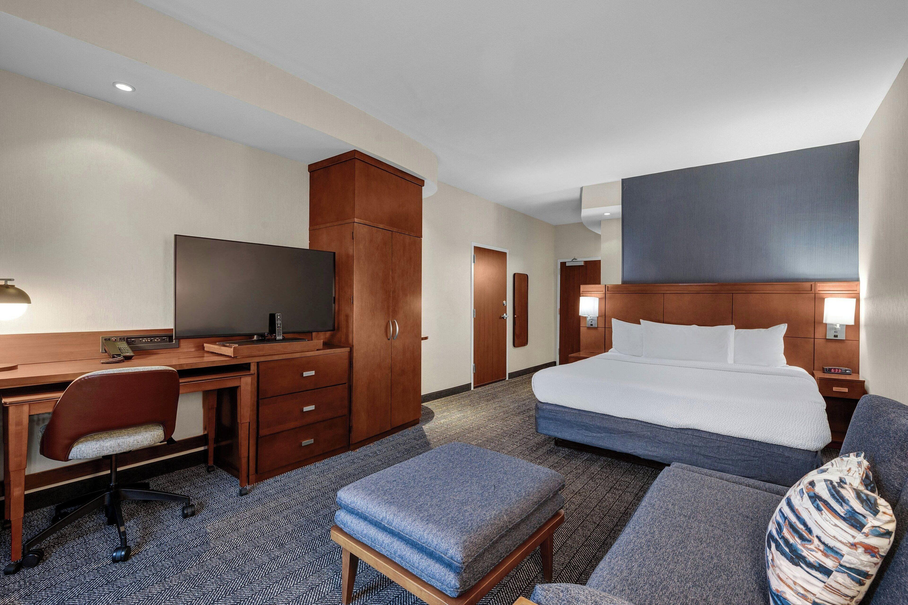 Una habitación de hotel con cama, escritorio, silla, televisor y armario.