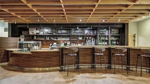 Un espace bar avec un plafond en bois, des tabourets de bar, un comptoir avec un menu et des étagères remplies de bouteilles.