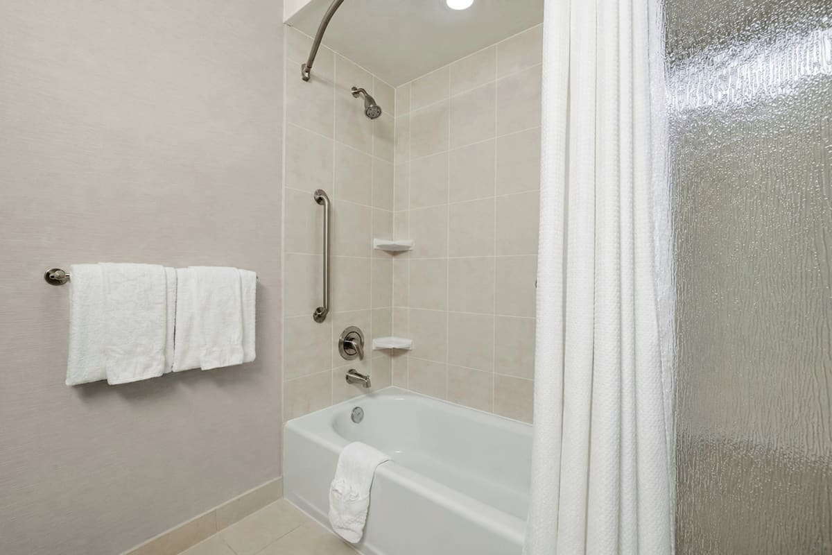 A bathroom with a bathtub, a shower, and a handrail.