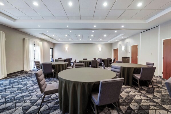 Una sala conferenze con tavoli e sedie rotonde, una moquette decorata e luci a incasso nel soffitto.