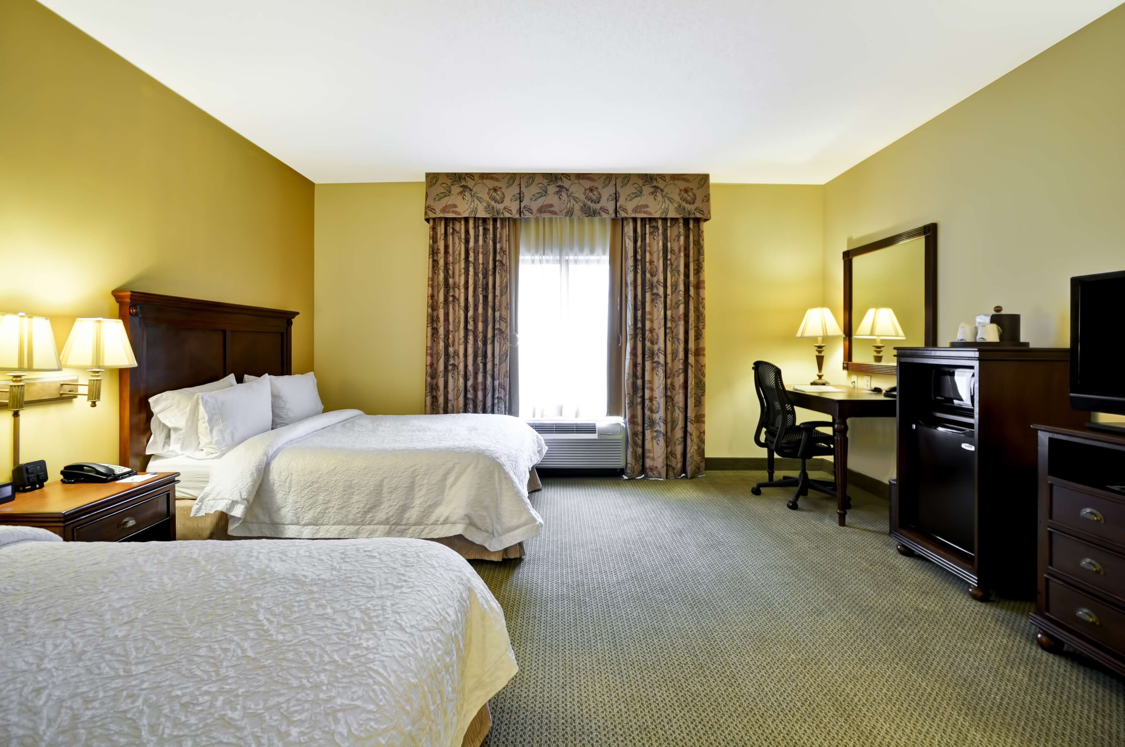 A hotel room with two beds, a desk, a chair, a television, and a mirror.
