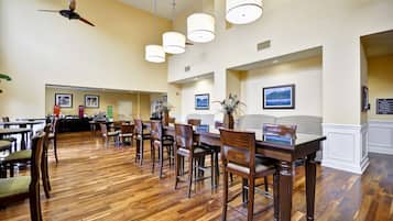 A spacious dining area with wooden flooring, multiple tables, and chairs.