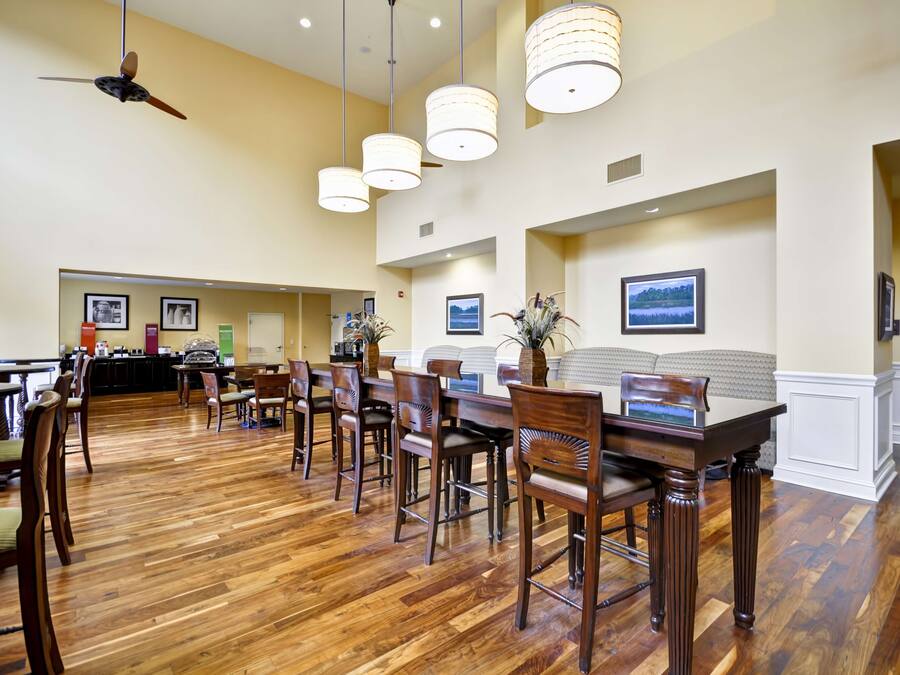 A spacious dining area with wooden flooring, multiple tables, and chairs.