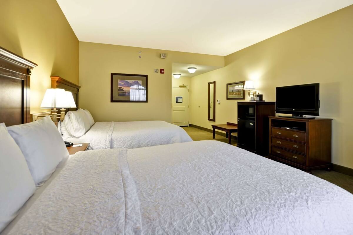 A hotel room with two beds, a TV, a desk, and a lamp.