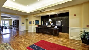 Una zona de recepción con suelo de madera, un mostrador de recepción, cuadros enmarcados en la pared y una alfombra roja con texto.