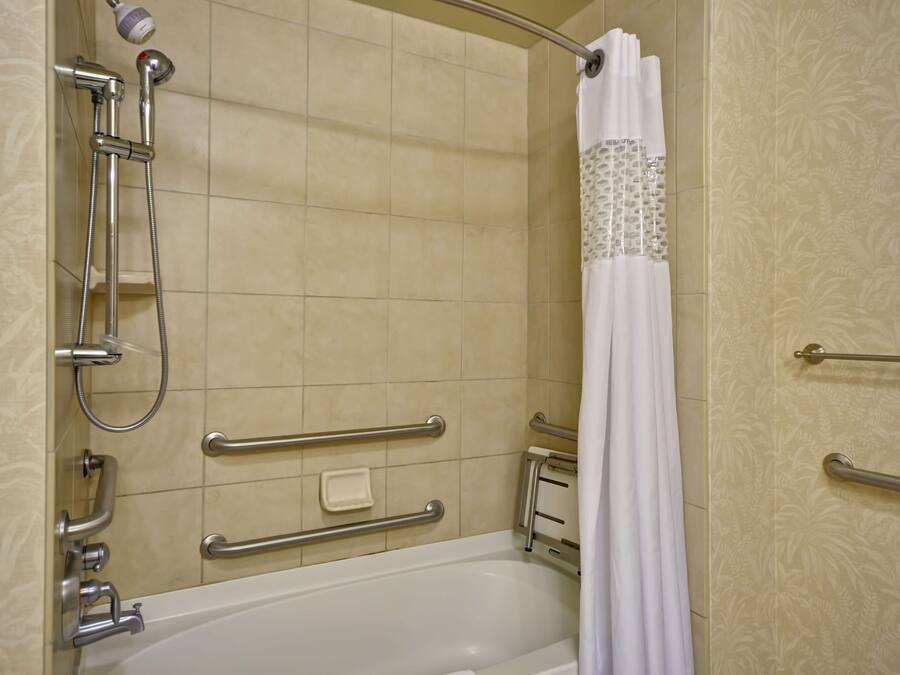 A bathroom with a bathtub, shower, and handrails.