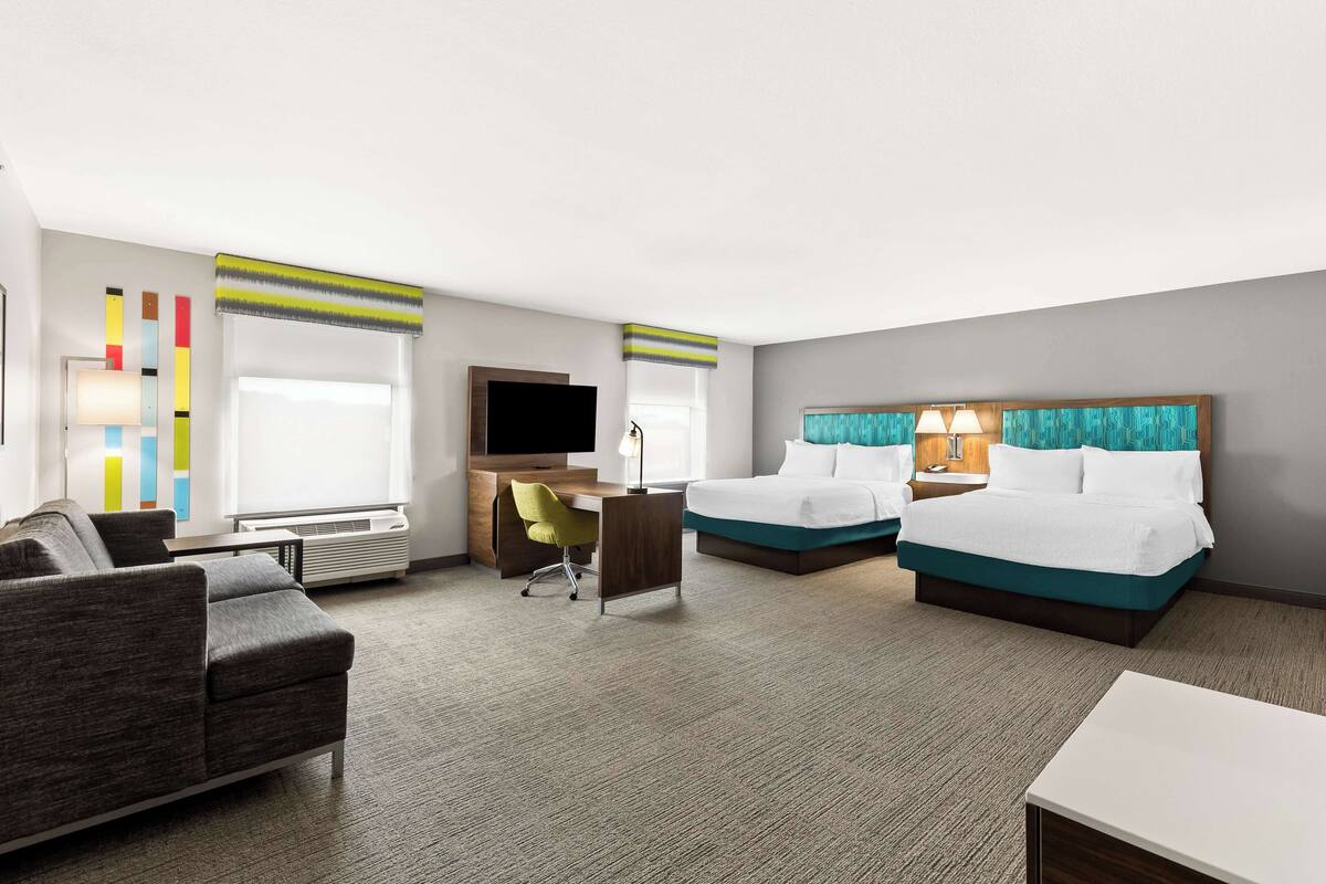 A hotel room with a sofa, two beds, a desk, and a TV.